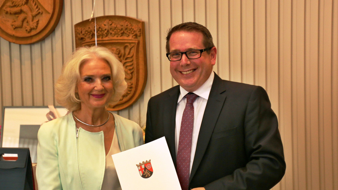 Links im Bild ist Frau Höh-Eymael die von Herrn Linnertz dem Präsidenten der Aufsichts- und Dienstleistungsdirektion die Urkunde überreicht bekommt. Herr Linnertz steht rechts