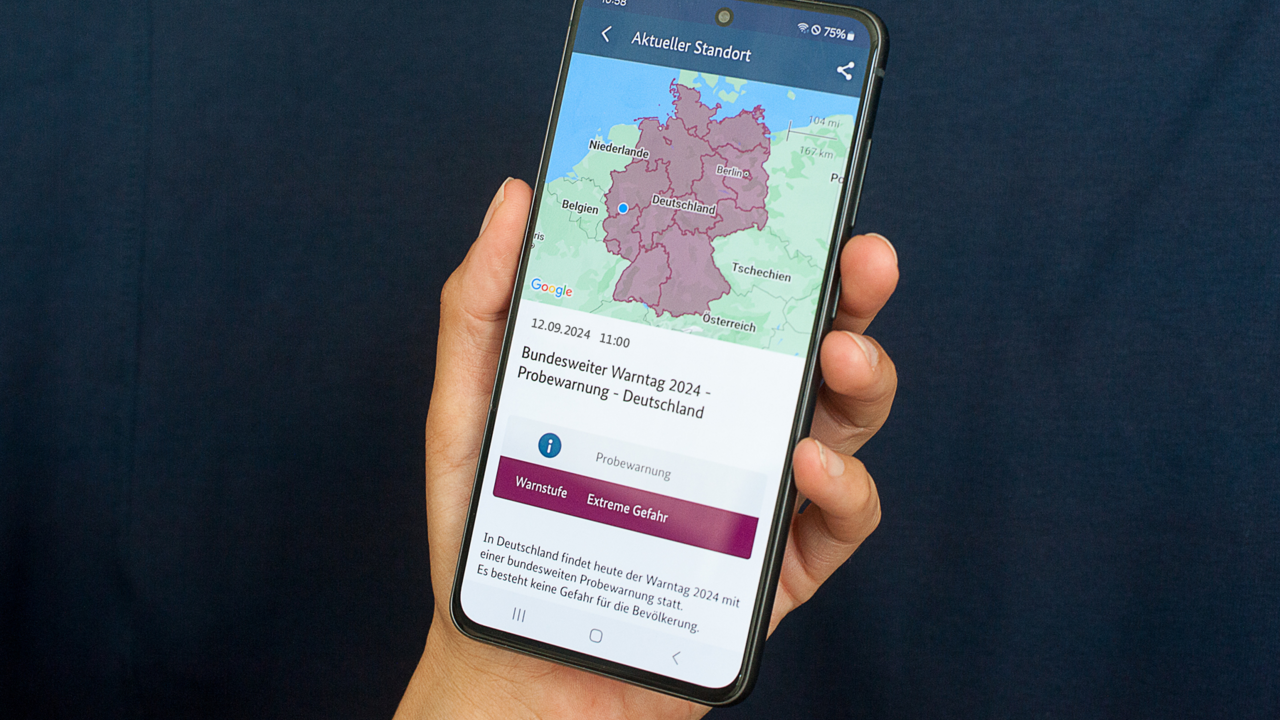 Symbolbild zum bundesweiten Warntag 2024 - ein Hand die ein Mobiltelefon festhält mit der Aufschrift bundesweiter Warntag 2024 und einer Karte